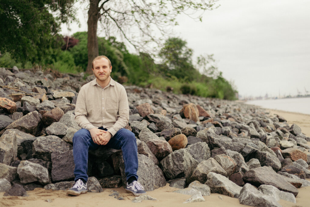 Fynn sitzt auf Steinen am Strand guckt in die Kamera